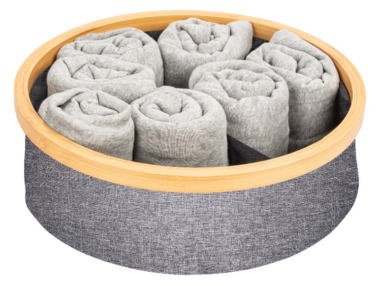 Des vêtements roulés dans un panier gris avec un bord en bambou.