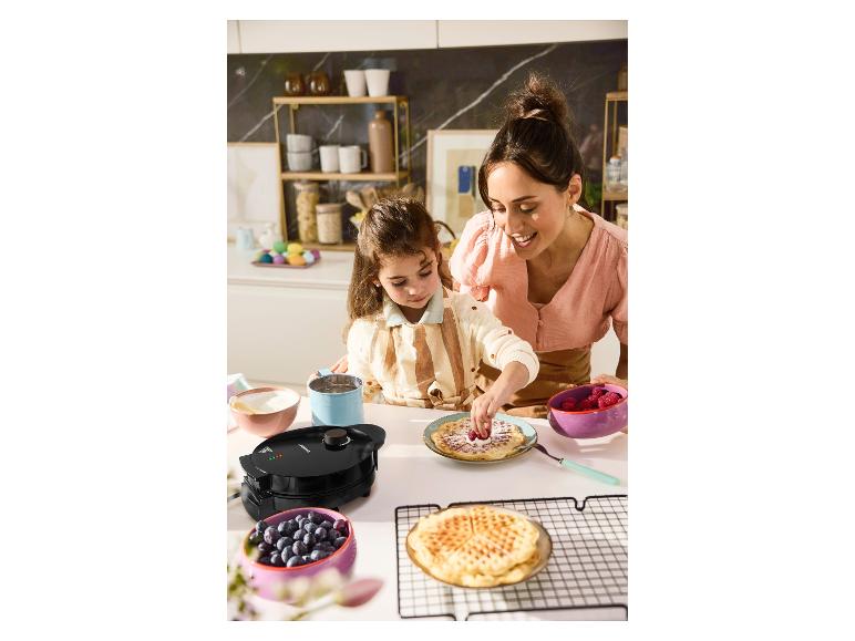 Mère et fille décorent des gaufres avec des fruits rouges et des myrtilles, à côté d'un gaufrier.