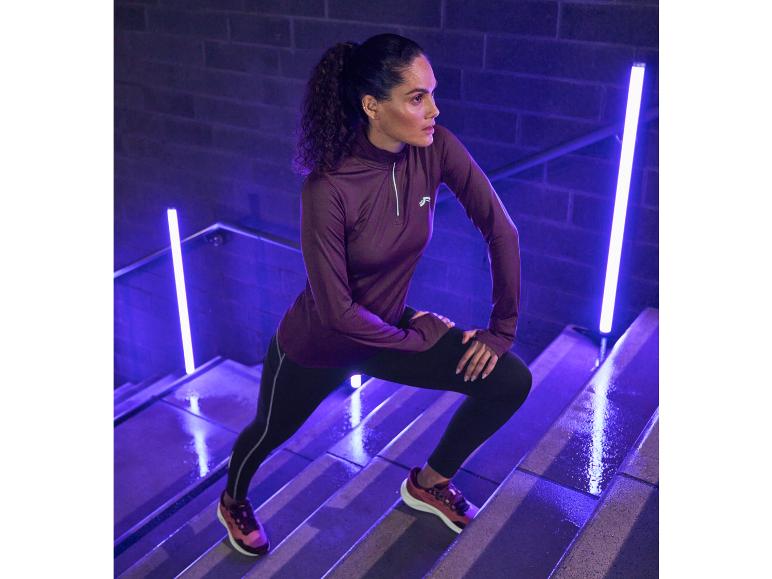 Une femme vêtue de vêtements de sport Reebok, dont un sweat-shirt violet et un legging noir, s'entraîne sur un escalier.