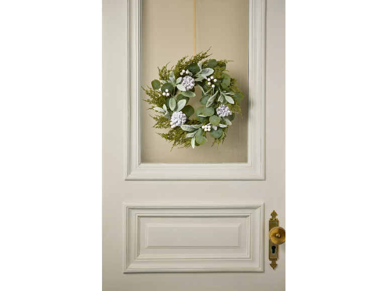 Couronne d'hiver avec feuillage vert, baies blanches et pommes de pin sur une porte.