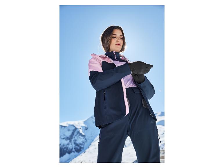 Femme en veste et pantalon de ski, ajustant ses gants sur une piste ensoleillée.
