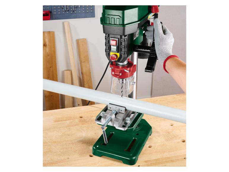 Perceuse à colonne Parkside perçant un tuyau fixé par un étau sur un établi en bois.