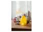 Une lampe en verre jaune en forme d'œuf sur une table en bois avec des œufs et des fleurs.