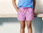 Un enfant porte un short rose à imprimé coquillages.