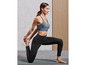 Une femme en soutien-gorge de sport bleu et leggings noirs fait du yoga sur un tapis vert.