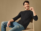 Un homme assis sur une chaise avec un pull noir et un jean.