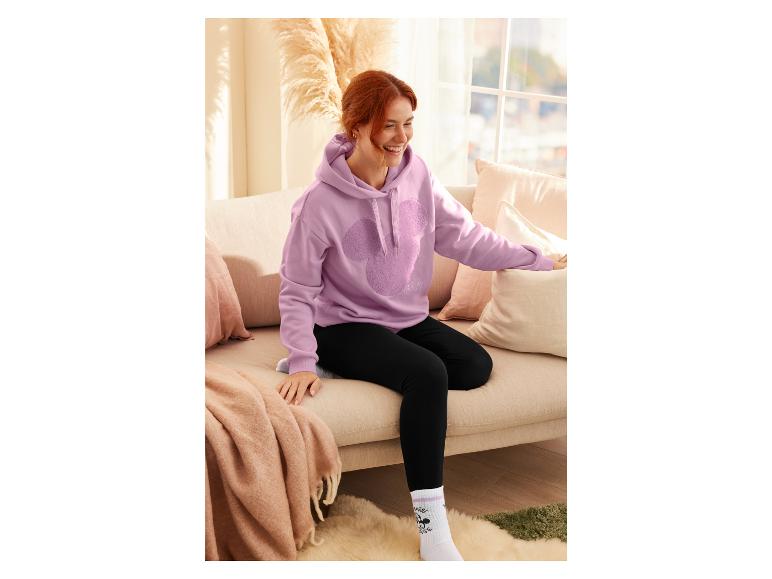 Une femme portant un sweat-shirt rose à l'effigie de Mickey Mouse est assise sur un canapé.