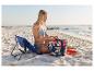 Femme en maillot de bain assise sur une chaise pliante à la plage, avec un sac de plage.
