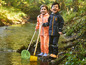 Deux enfants en vêtements de pluie avec un filet et une pelle près d'un ruisseau.