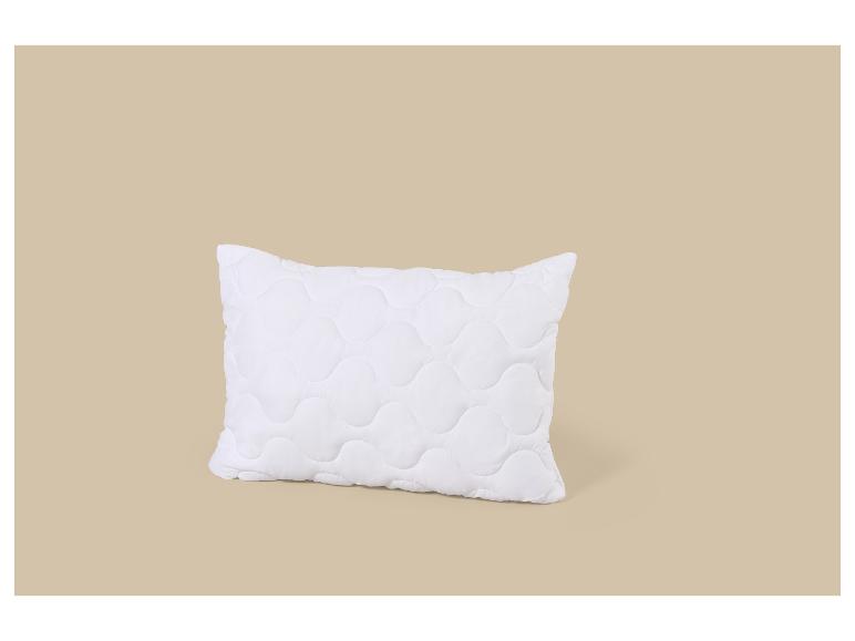 Oreiller blanc matelassé avec un motif ondulé sur fond beige.