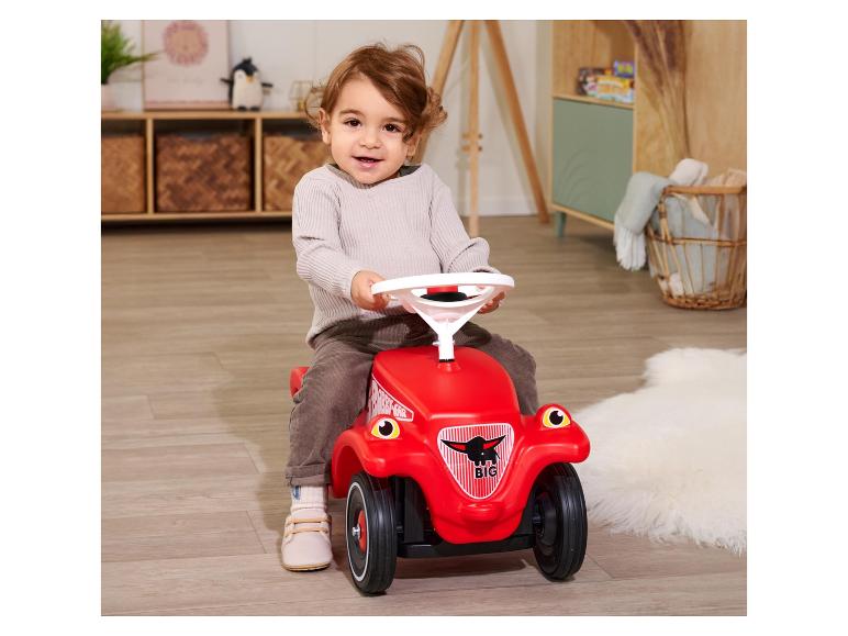 Bébé assis sur une voiture à pousser rouge dans une chambre d'enfant.