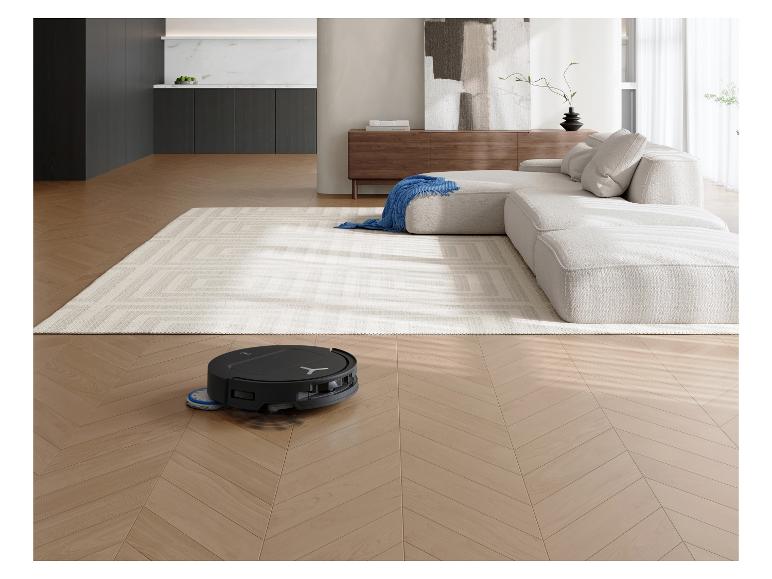 Robot aspirateur nettoyant un sol en bois dans un salon moderne avec canapé et tapis.