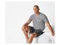 Homme portant un t-shirt gris et un short à carreaux.