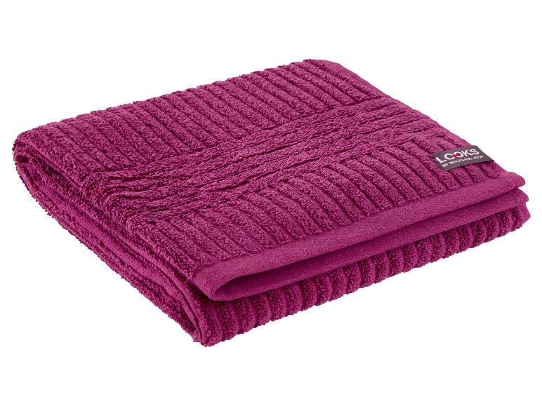 Serviette de bain magenta pliée avec un motif texturé et une étiquette noire.