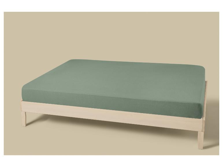 Lit en bois clair avec matelas recouvert d'un drap-housse vert