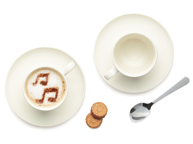 Une tasse de cappuccino avec des notes de musique, une tasse vide et une cuillère, à côté de deux biscuits.