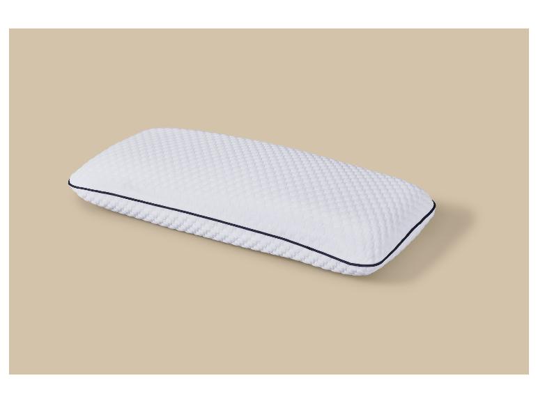 Oreiller blanc avec une surface texturée et un passepoil bleu foncé sur fond beige.