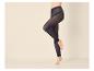 Jambes de femme en collants noirs transparents, une jambe levée, sur fond clair.