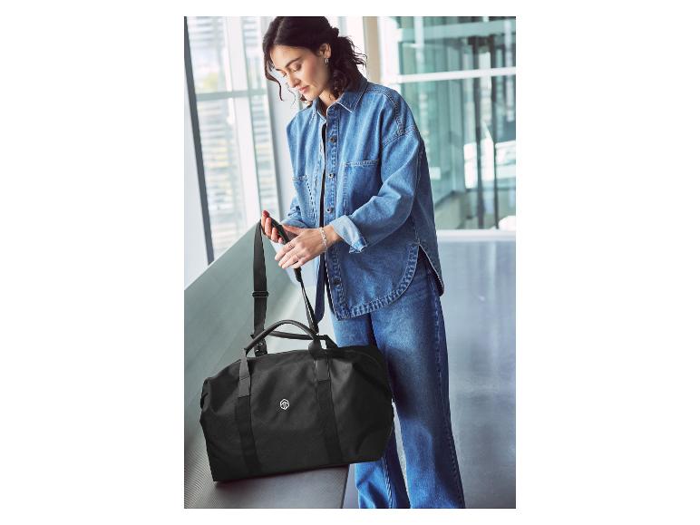 Une femme portant une veste en jean inspecte un sac de voyage noir.