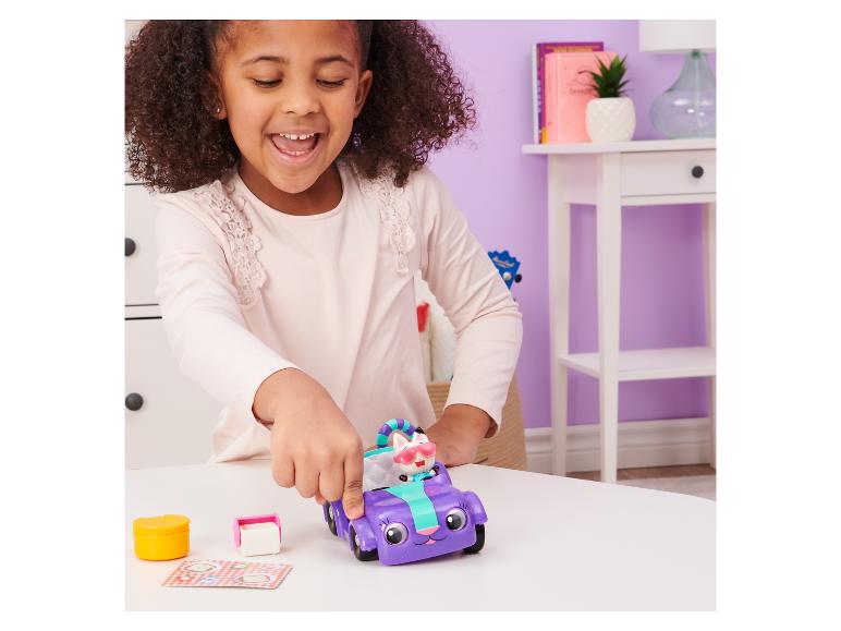 Une fille joue avec un véhicule jouet violet et une figurine de chat sur une table.
