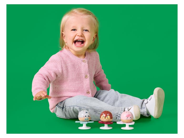 Bébé joyeux en cardigan rose et jean, jouant avec trois hochets colorés.