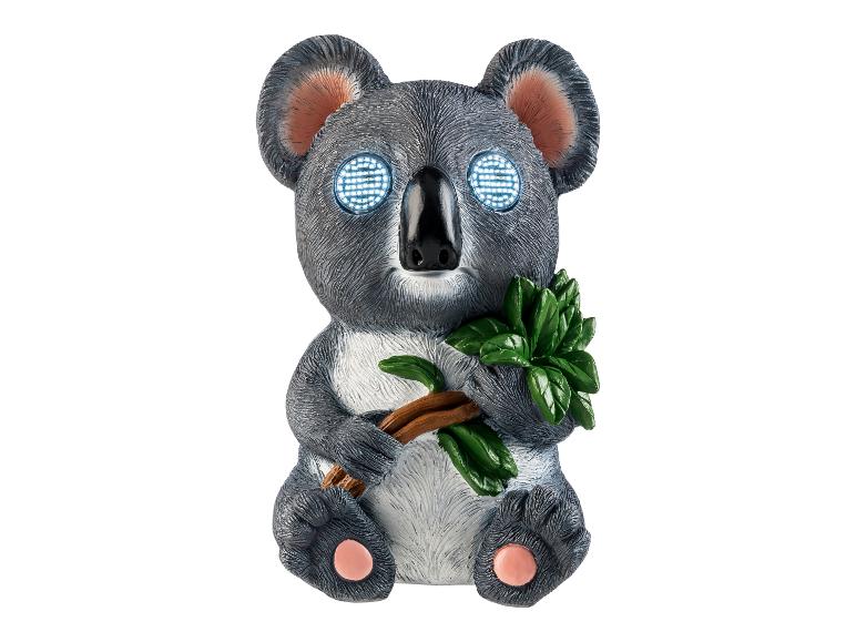 Figurine de koala aux yeux lumineux et branche d'eucalyptus.