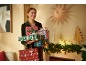 Femme souriante tenant une pile de cadeaux de Noël et un sac avec le texte « Merry Christmas ».