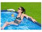 Femme souriante dans une piscine avec maillot de bain et lunettes de soleil, tenant un verre de boisson.
