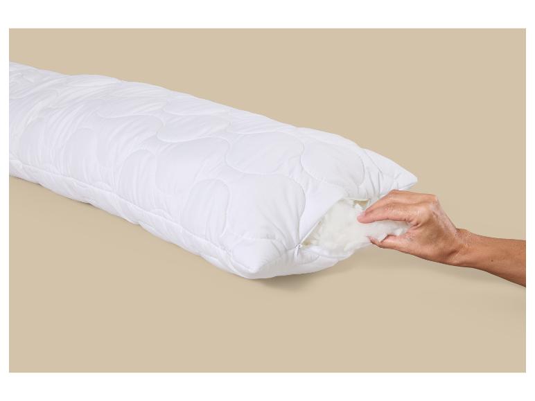 Oreiller blanc matelassé avec fermeture éclair, une main ajuste le rembourrage.