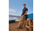 Homme en polo marine et pantalon beige sur la plage avec des bateaux.