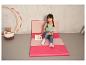 Une fille assise sur un tapis de jeu rose en train de lire un livre.
