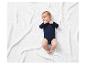 Bébé en body bleu marine sur une couverture blanche tricotée.