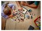 Deux personnes construisent des ensembles LEGO Ninjago sur une table en bois, utilisant une tablette pour les instructions.