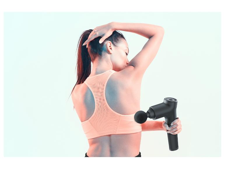 Une femme en brassière de sport utilise un pistolet de massage pour la récupération musculaire.