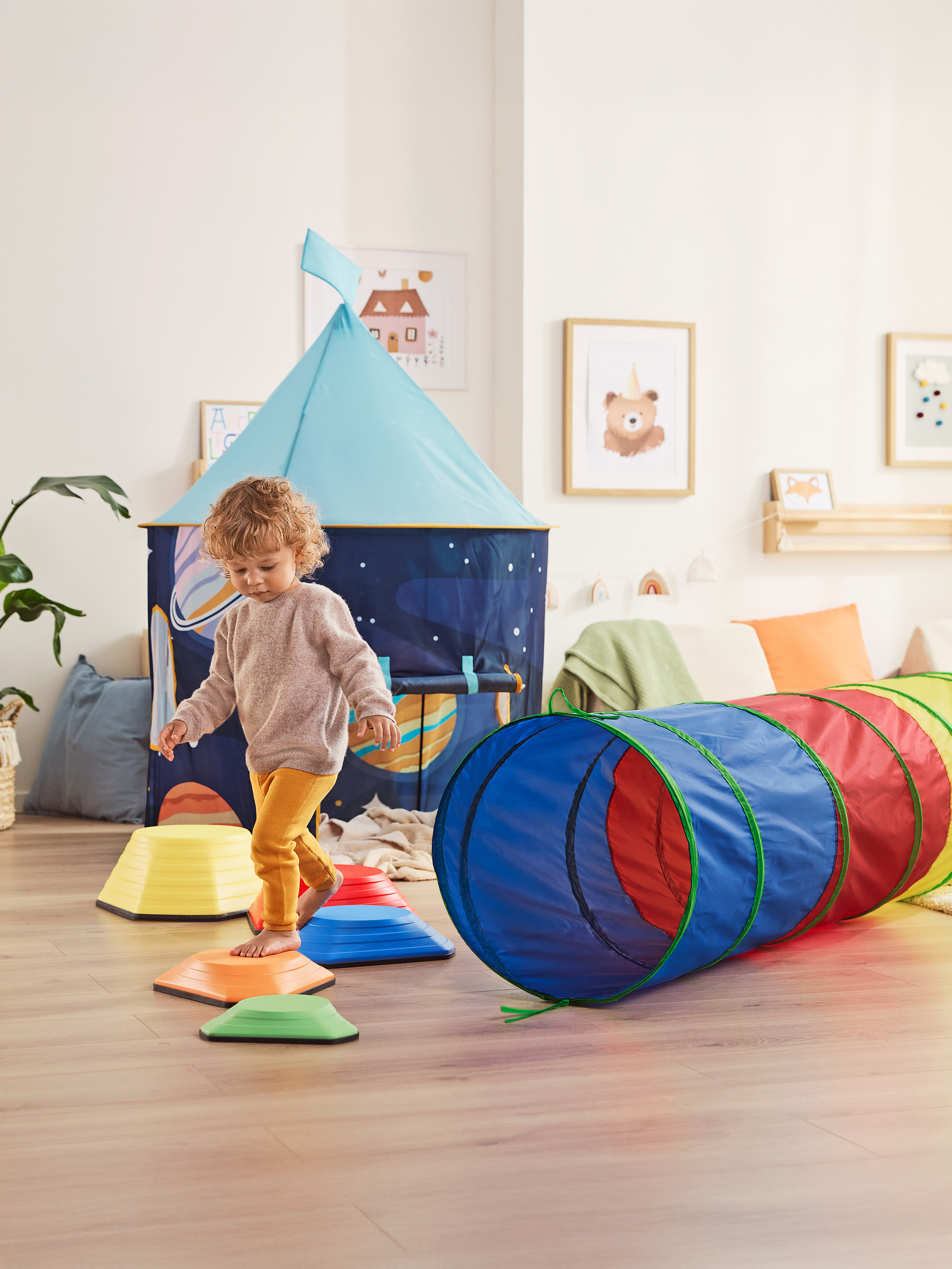 Enfant jouant avec un tunnel de jeu coloré et des pierres d'équilibre dans une chambre d'enfant.
