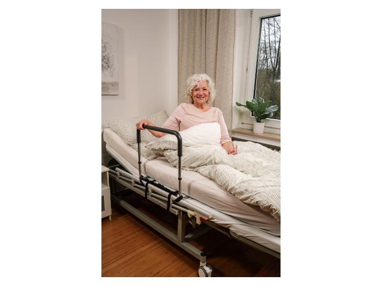 Femme âgée souriante assise dans un lit réglable avec une barrière de lit.