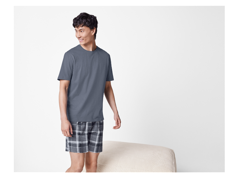 Homme portant un t-shirt gris et un short à carreaux.