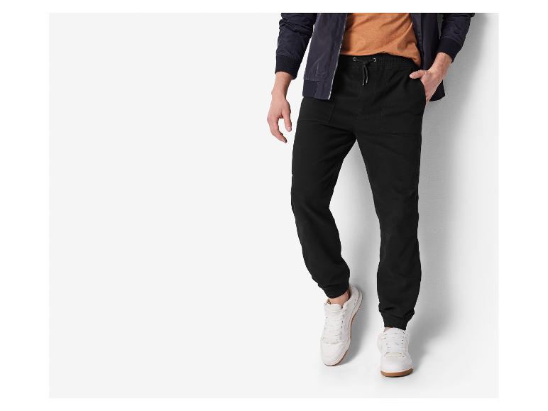 Homme en pantalon de jogging noir, t-shirt marron et blouson bomber bleu foncé.