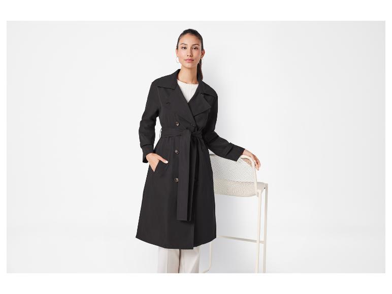 Une femme en trench-coat noir et pantalon blanc.
