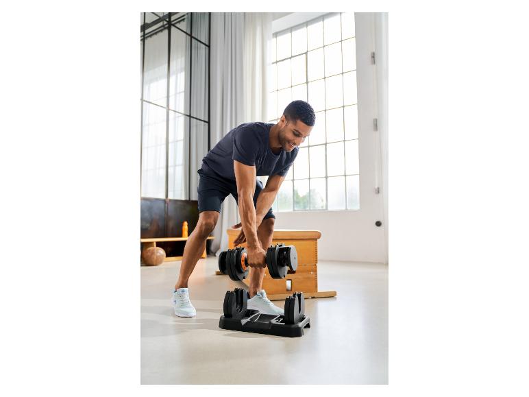 Homme souriant utilisant un haltère réglable dans un salon lumineux.