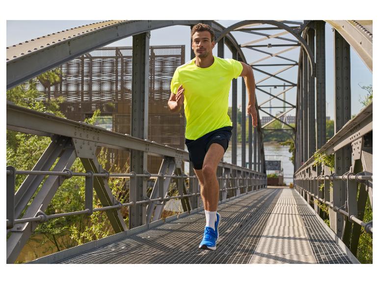 Un homme court sur un pont, vêtu d'un t-shirt jaune et de chaussures de course bleues.