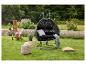 Fauteuil suspendu noir avec coussins, table d'appoint, pouf et chaise de jardin dans un jardin verdoyant.