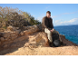 Homme en veste et pantalon de randonnée assis sur des rochers au bord de la mer avec un sac à dos.