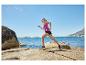 Femme courant en débardeur et short de sport sur une côte rocheuse.