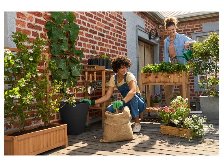 Deux femmes jardinent sur un balcon avec des jardinières en bois et des outils de jardinage.