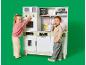 Deux enfants jouant avec une grande cuisine en bois pour enfants sur fond vert.