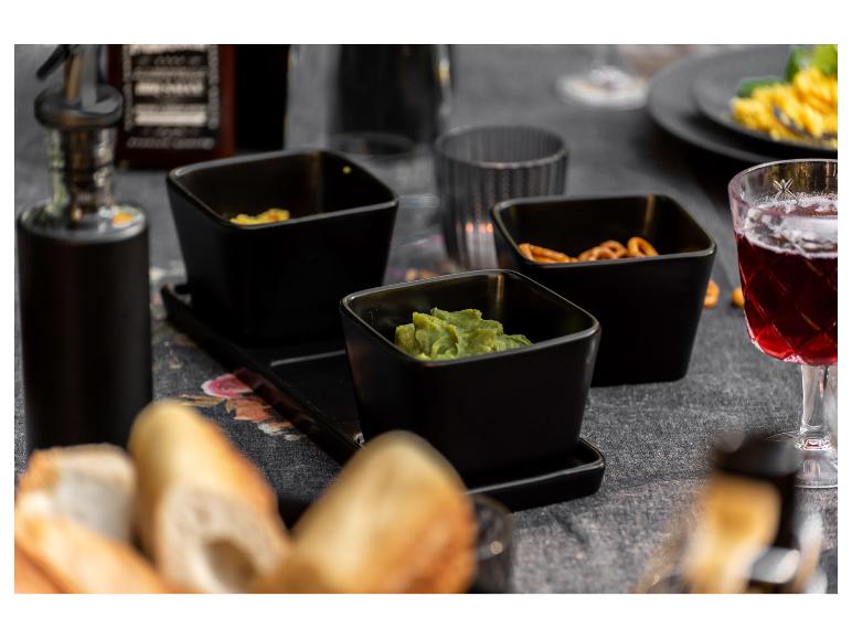 Bols noirs avec du guacamole, des bretzels et des baguettes sur une table.