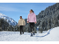 Deux personnes en vestes et pantalons d'hiver marchant dans un paysage de montagne enneigé.