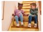 Deux enfants en hauts colorés à manches longues, leggings et baskets assis dans les escaliers.