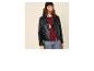 Femme en veste en cuir noire, pull argyle rouge, jean et bonnet noir.